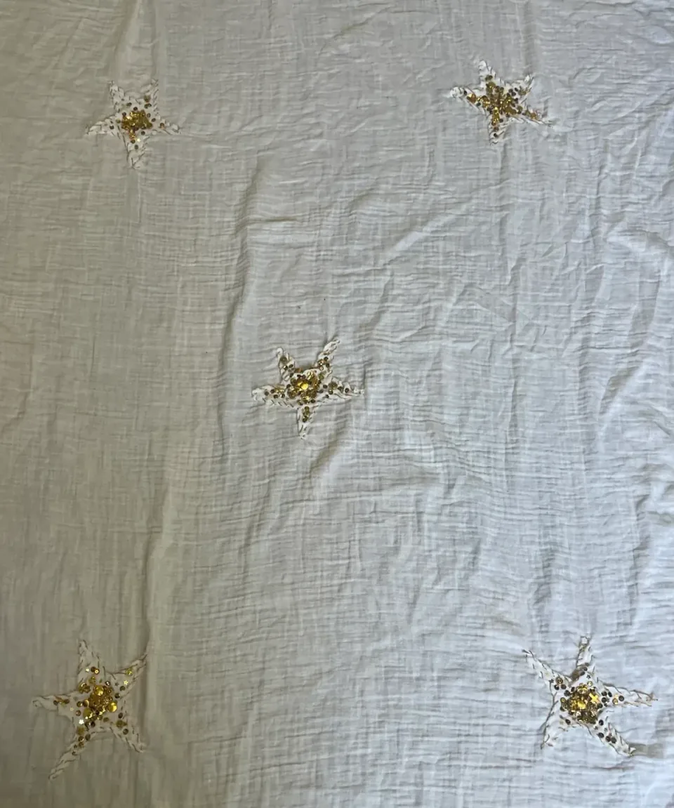 Photograph of a white fabric panel with five embroidered stars spread across it, each with a cluster of sequins and beads at the centre.